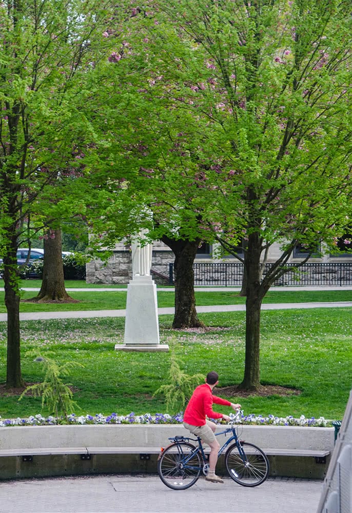 A student rides on a bike looking at a statue in the background