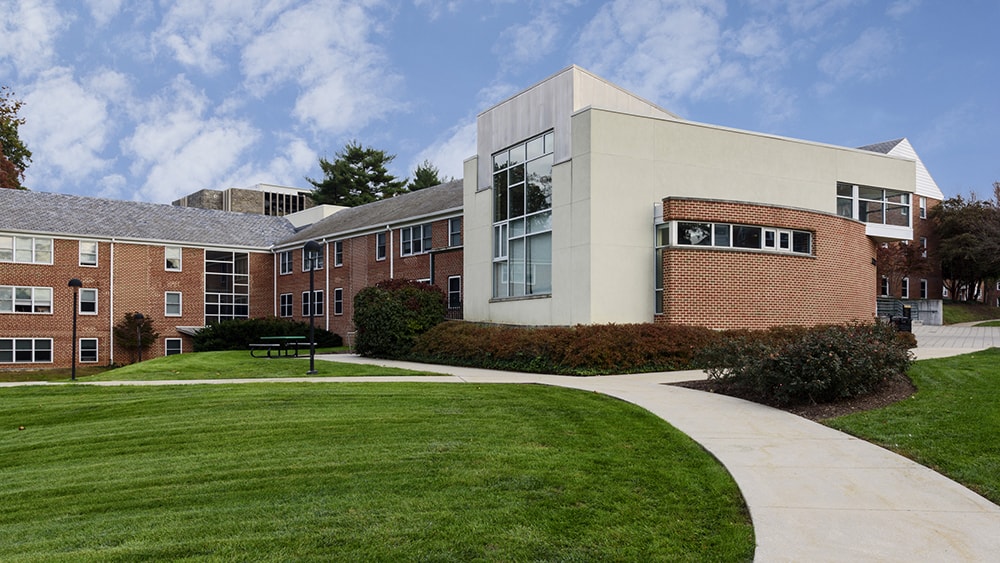 One of the residence halls on the west side of campus with green grass in front and a blue sky above