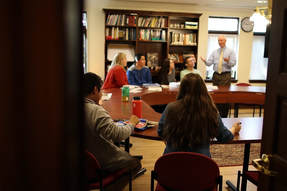 Several students sitting around a small circular table listening to a lecture