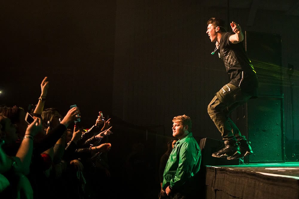 A music performer jumps on stage and the crowd cheers with their hands in the air