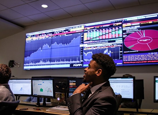 Male student in suit sitting in front of multiple TV monitors