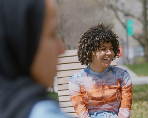 Students smile and laugh while they have a chat on the lounge chairs on the quad lawn