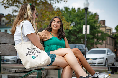 Two students having a conversation on a bench in Fells Point, Baltimore on a sunny day