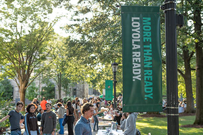Many students walking through the quad by a banner reading "More than ready. Loyola ready."