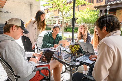 Group of students doing schoolwork together on a patio on a bright, sunny day