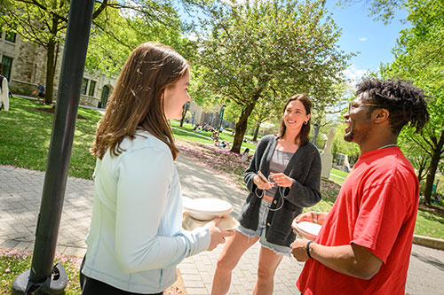 Three students smiling in conversation while standing by the bright green quad