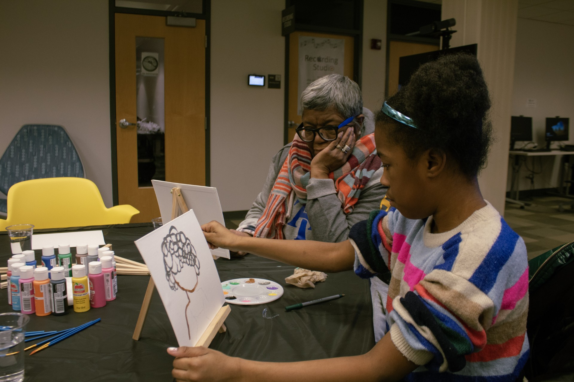 A young girl painting a picture of a girl with an afro