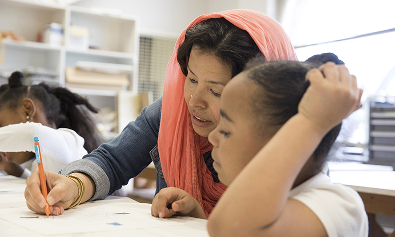 Adult female writing while the child sitting beside her watches