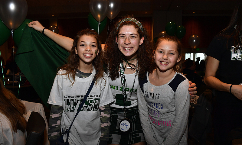 A female Loyola athlete posing for a photo with two young girls