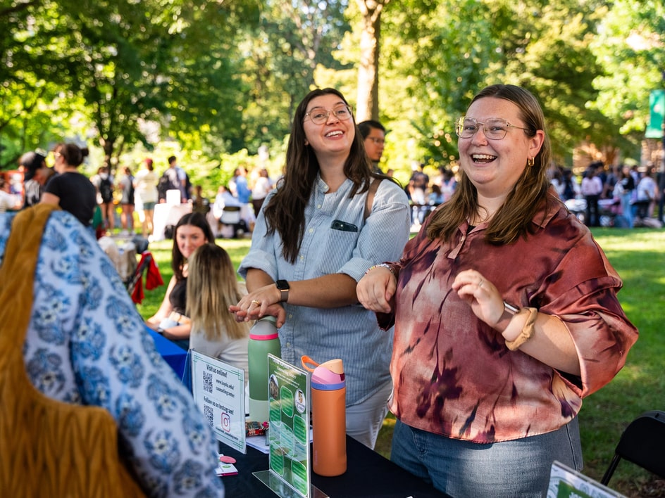 Two students smiling and laughing at a tabling event outdoors