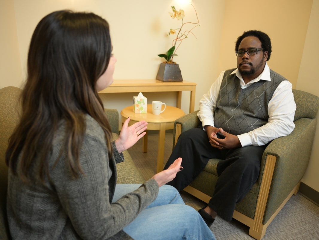 The back of a student's head as she engages with a counselor who listens carefully with hands folded.