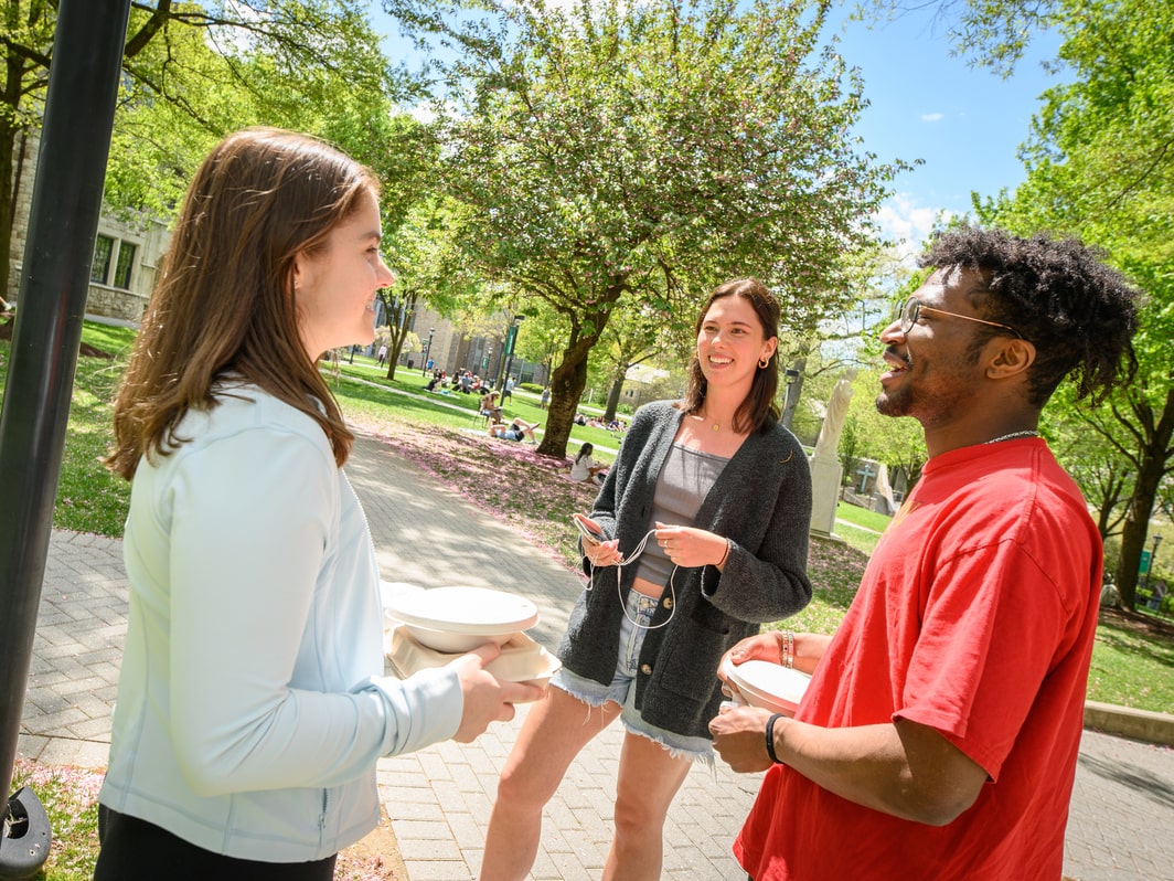 Three students smile and engage in conversation outside on the quad
