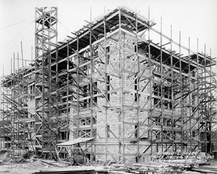 Historic photograph of a large, three-floor, stone building, covered in scaffolding
