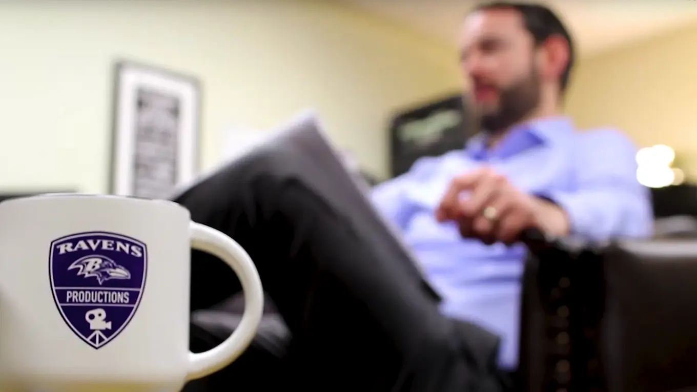 A mug with "Ravens Productions" on it, with a man sitting in a seat blurred in the background - Press enter to play