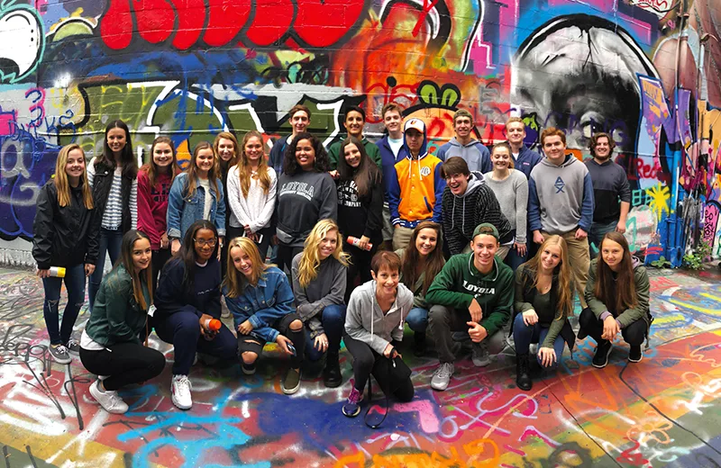 Students pose for a picture in front of a wall covered in bright graffiti
