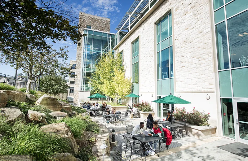 Students eat at tables outside of a building with white brick