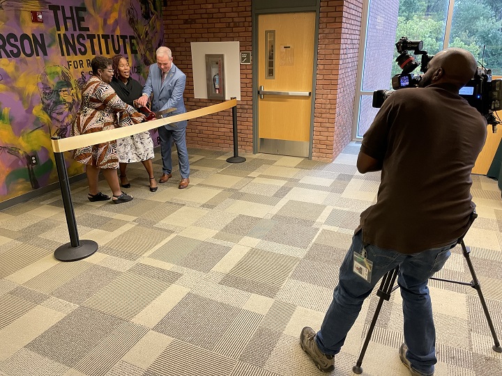 Three people cut a ribbon to celebrate the opening of the new space for the Karson Institute