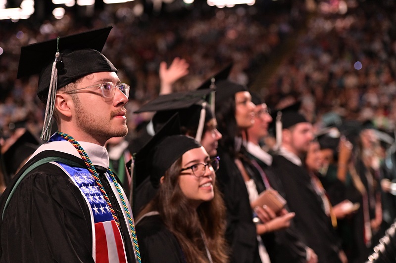 Members of the Class of 2023 stand and look toward the stage at their Commencement