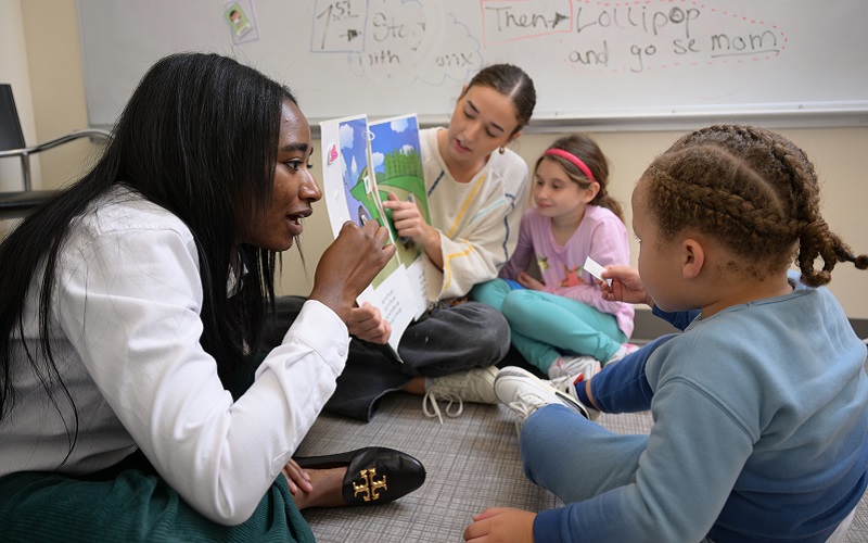 Two graduate students sit on the floor reading and speaking to children in the Loyola Clinical Centers