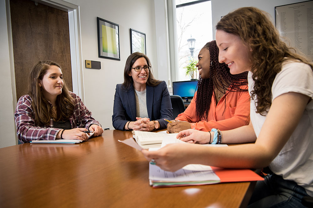 Marianna E. Carlucci, Ph.D., chair and professor of psychology, sits at a table with three Loyola students