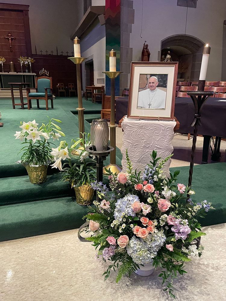 A portrait of Pope Francis with candles and flowers in Alumni Memorial Chapel.