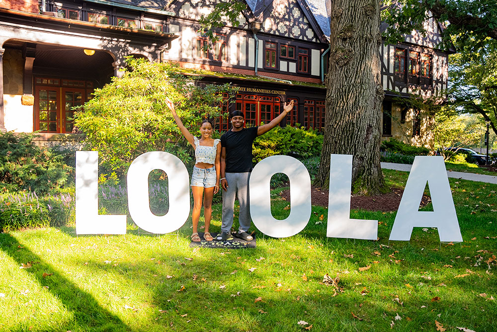 Students with a "Loyola" sign in front of the Humanities Center at the Fall 2025 Student Activities Fair
