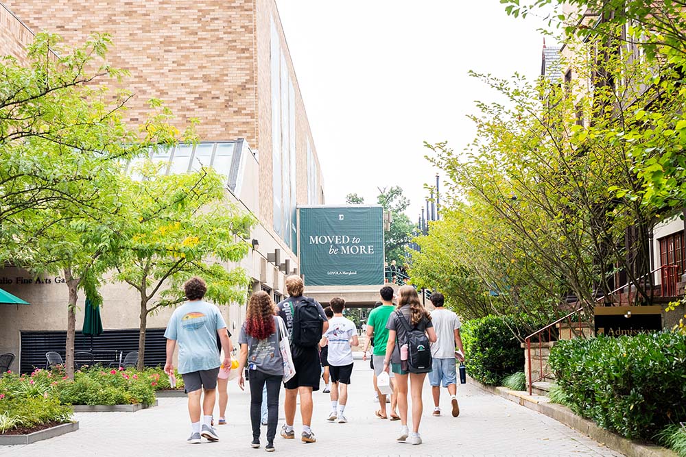Students walk on campus in front of a Moved To Be More sign in front of them