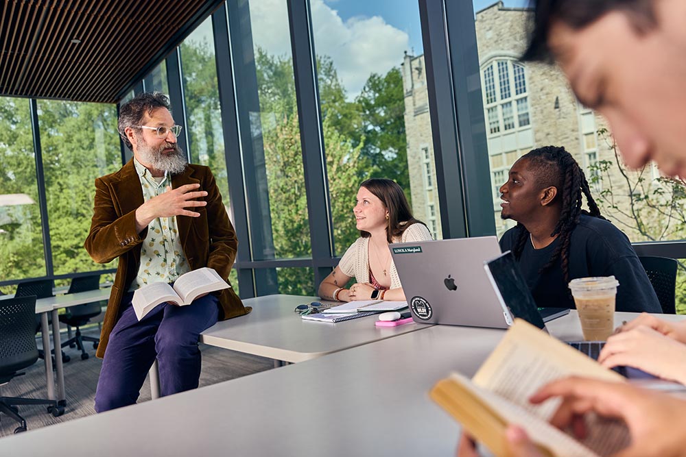 Professor talks with three students in classroom