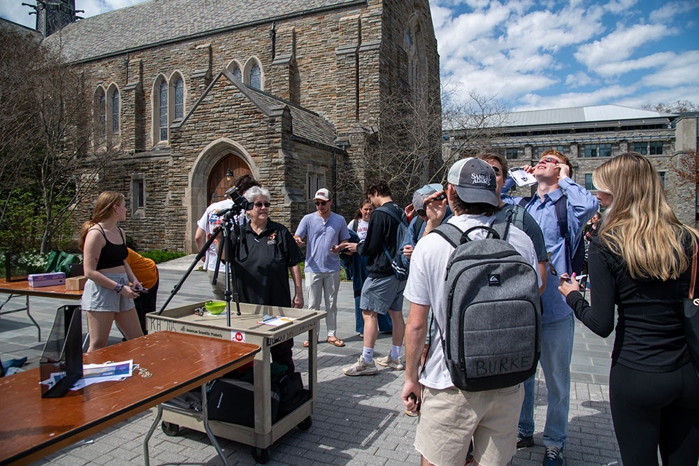 Heyer (middle) stands next to a solar scope with a group of students outside Loyola's Alumni Memorial Chapel during the Great North American Eclipse on April 8, 2024