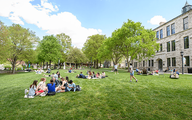 An expansive quad lawn stretches under a partly cloudy sky with students enjoying the weather
