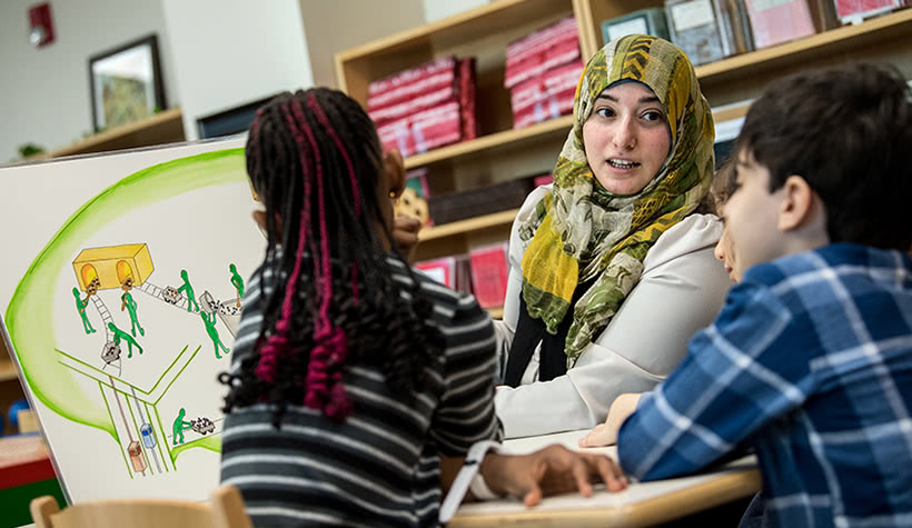 A group of students sitting at a table listening to their teacher