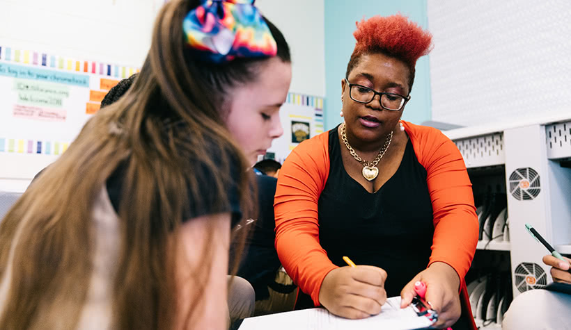 A teacher writing in a notebook as a student reads along