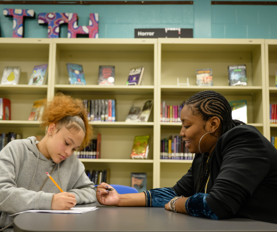 A female teacher works at a table with a female student on work.