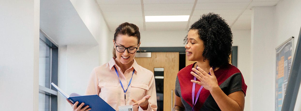 Two female administrators talk while walking down a hallway