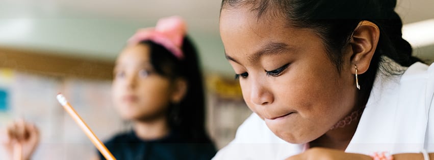 A young female student holding a pencil in a classroom