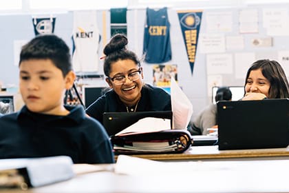 Students smiling and working on laptops in a classroom