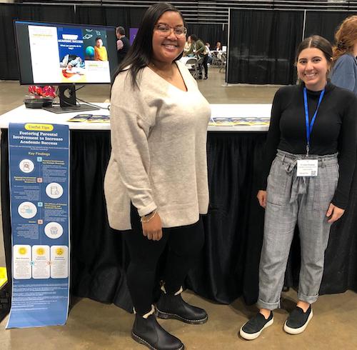 Two woman standing proudly in front of a table with a research poster