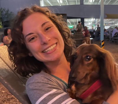 Woman with brown, curly, shoulder-length hair holding a dog with a red collar