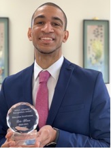 Headshot of man in suit holding a glass trophy that says MLEA Mnority Recognition Award