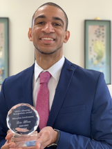 man in jacket and tie holding round glass trophy