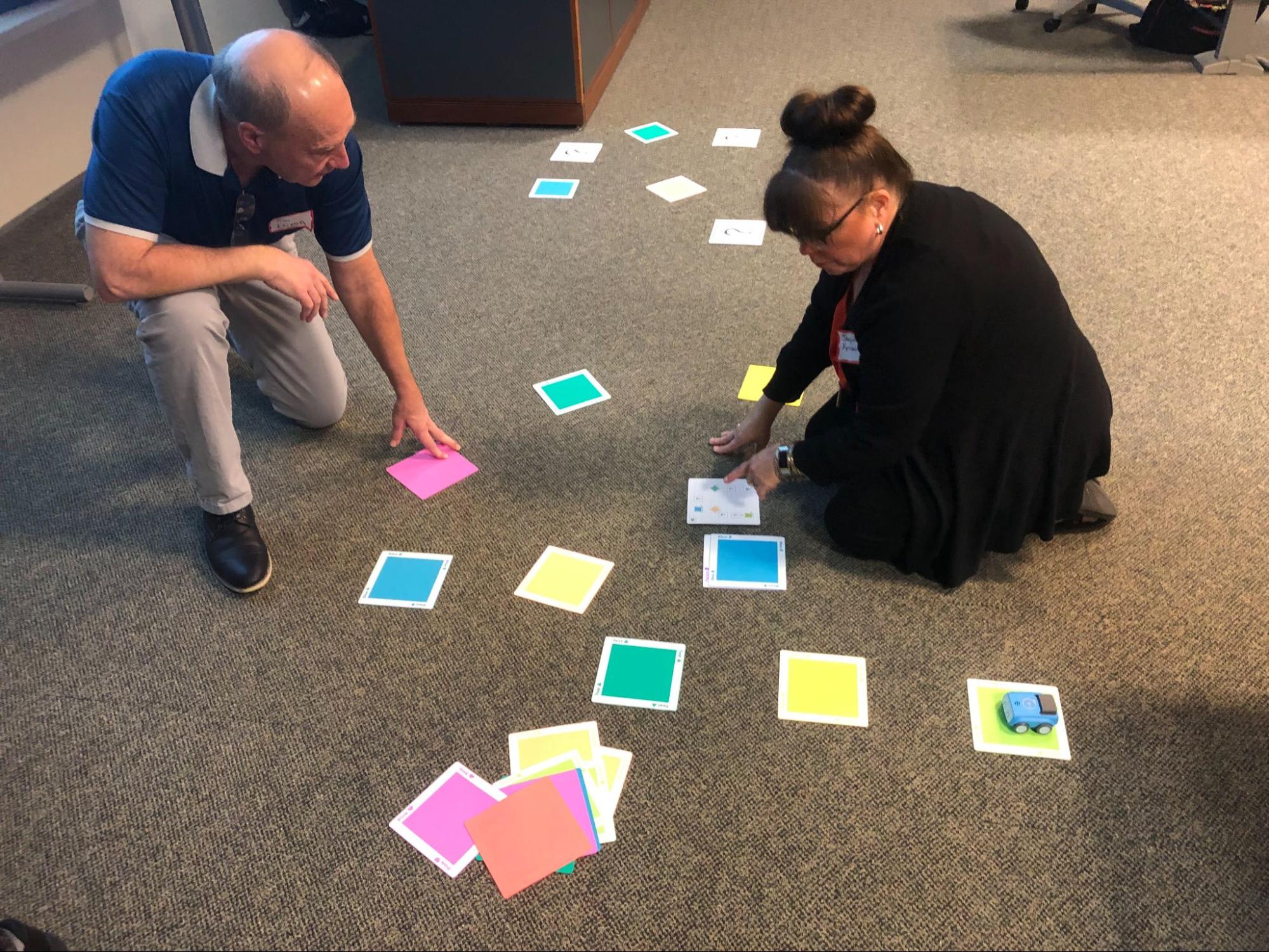 man kneeling and woman sitting on carpet with cards of various colors