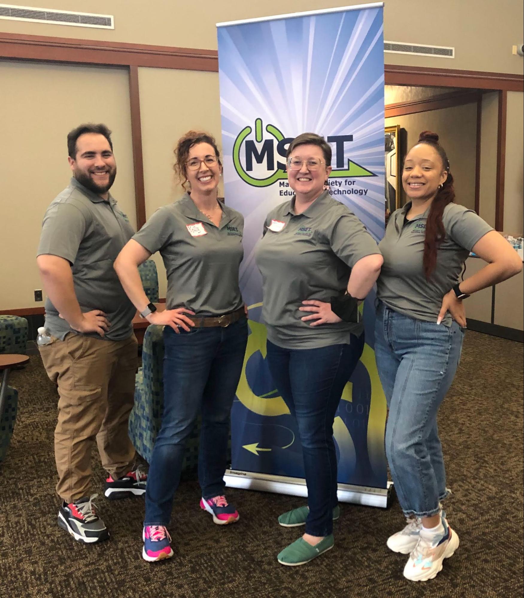 4 people in green shirts standing in front of a banner for the Maryland Society for Educational Technology