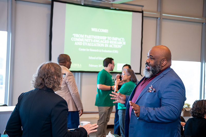 Two individuals talk while there is a presentation in the background. 