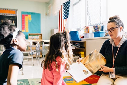 A teacher sitting on a classroom rug while reading to students