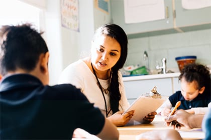 A female teacher sitting at a table instructing young students