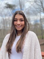 Abby Herman smiles in a white cardigan with wintery trees behind her