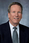 Bob Jirsa smiles for a portrait, wearing a suit and tie