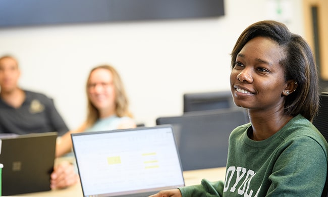 A student smiles at a desk listening to a seminar
