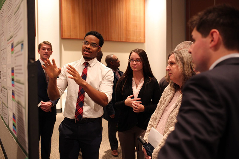 A student wearing business attire presenting a posted to a small group of people