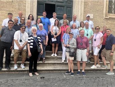 People gather for a photo outside of an old, white-bricked building